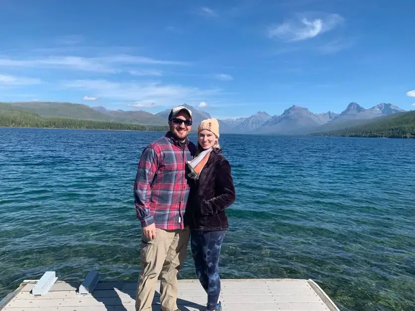 Husband and wife stand in front of calm water and mountain views