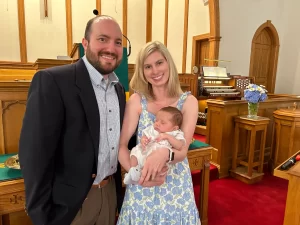 Man and woman posing for a picture with their baby in the front of church on father's day